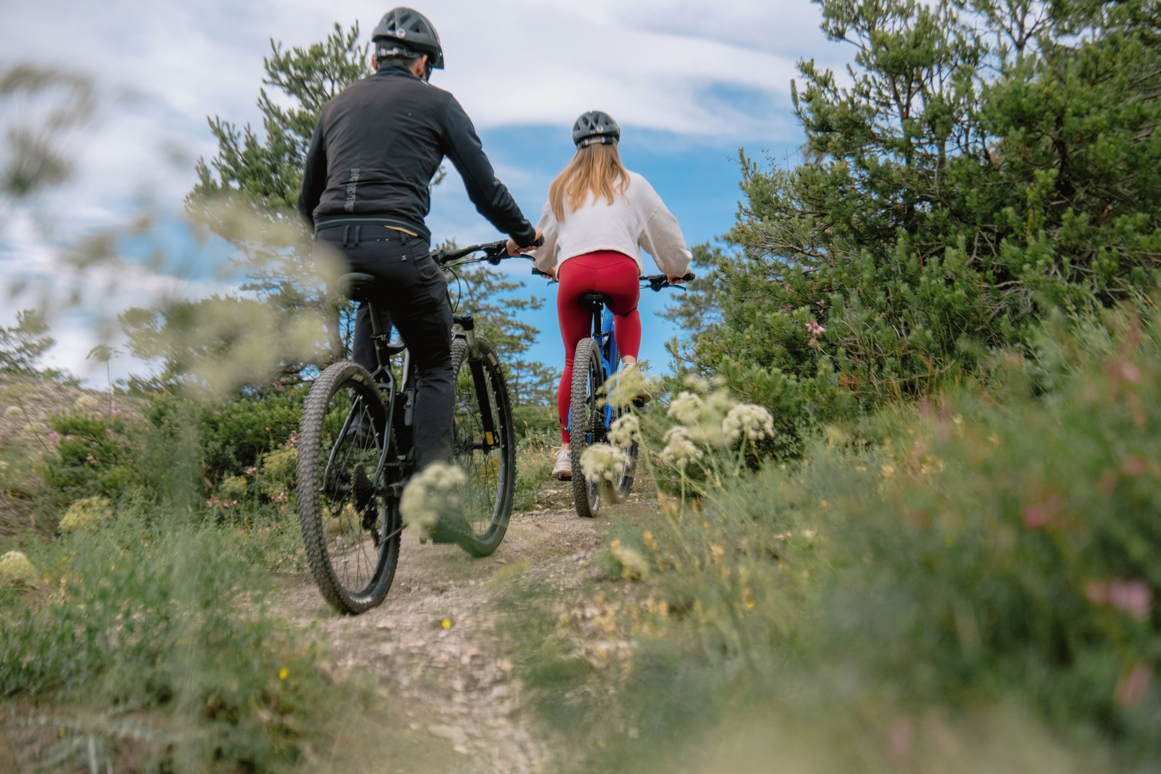 Two people on a mountain bike trail surrounded by greenery.