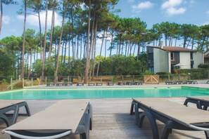 A swimming pool with lounge chairs, surrounded by tall trees and a building with a tiled roof. - Résidence Vacances Bleues Domaine de l'Agreou (Seignosse)