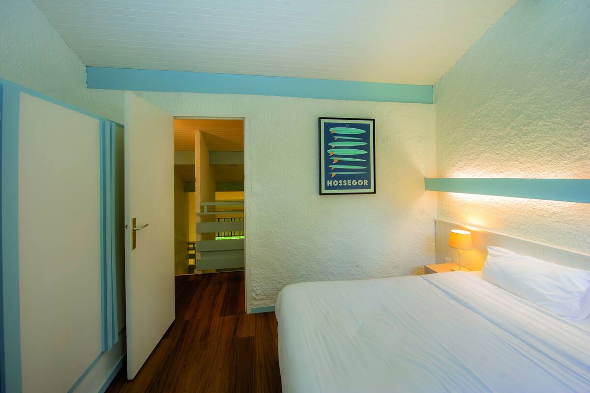 A hotel room with a bed, a nightstand, a wall-mounted lamp, and a framed picture on the wall.
