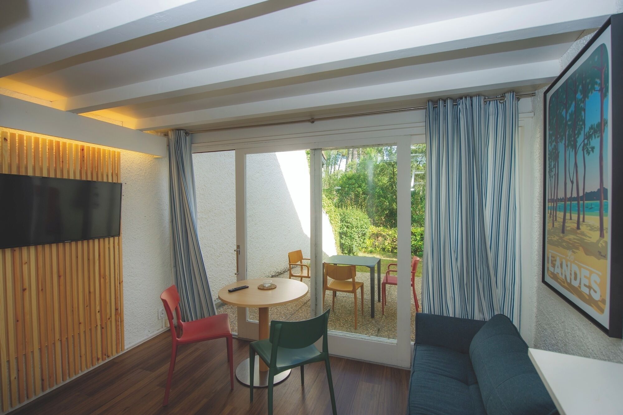 A room with a TV, a table with chairs, a sofa, and a sliding glass door leading to an outdoor area.