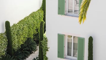 A white building with green shutters, a tiled roof, and a well-maintained garden with various plants and a pathway.