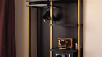Habitación de hotel con cama, armario con organizador para colgar, una caja de seguridad pequeña y escritorio con silla.