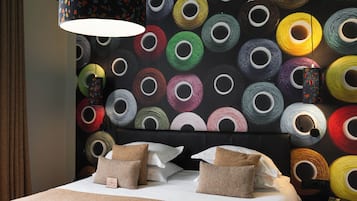 A neatly made bed with a clock, pillows, and a headboard in a room with a wall decorated with colorful circular patterns.