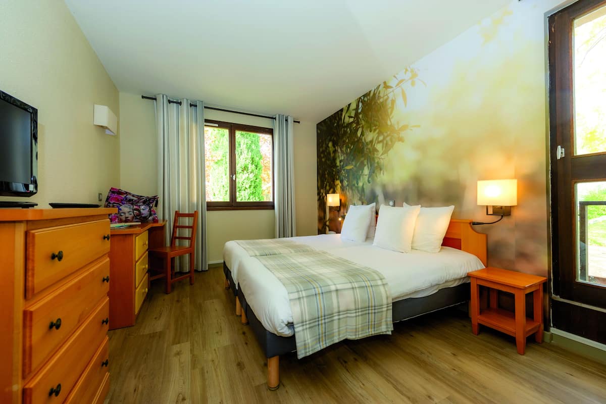A hotel room with a bed, wooden dresser, desk, chair, and a television.
