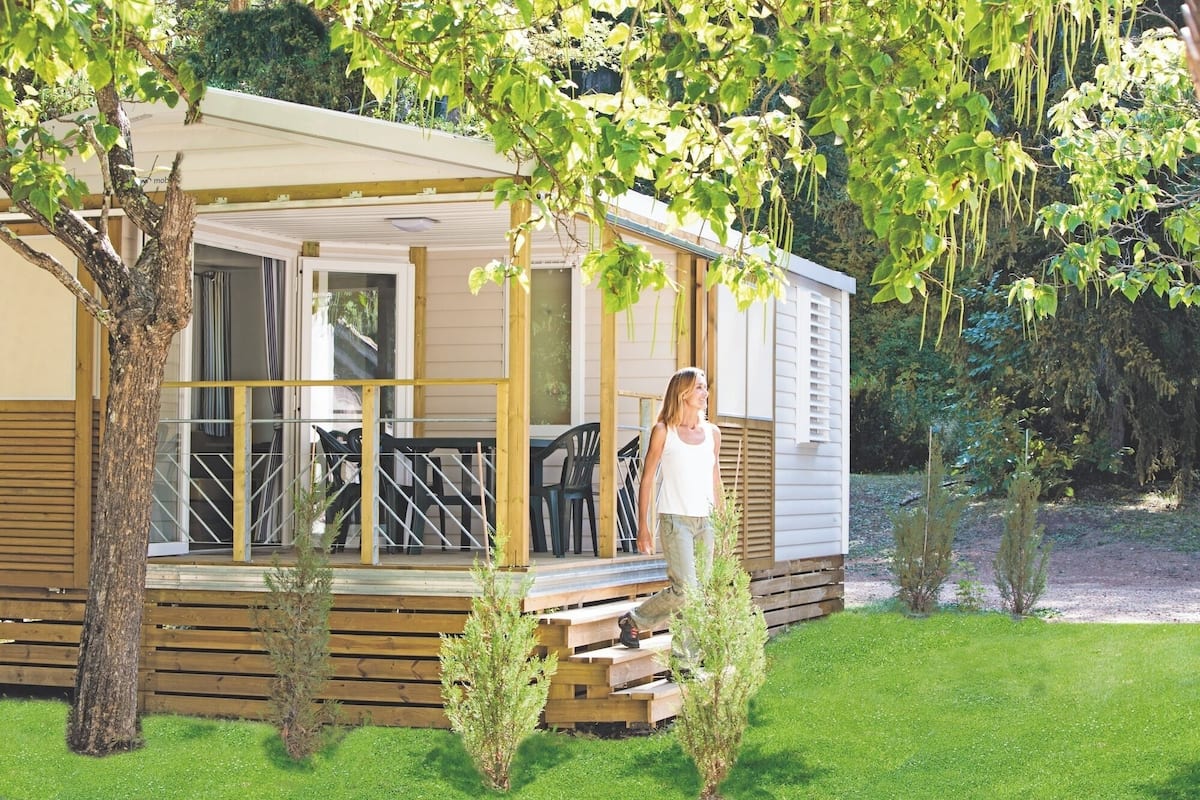 A mobile home with a porch, a small garden, and a tree.