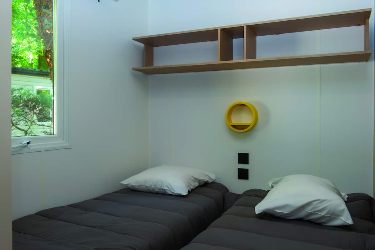 A bedroom with two beds, a window, and a shelf above the beds.