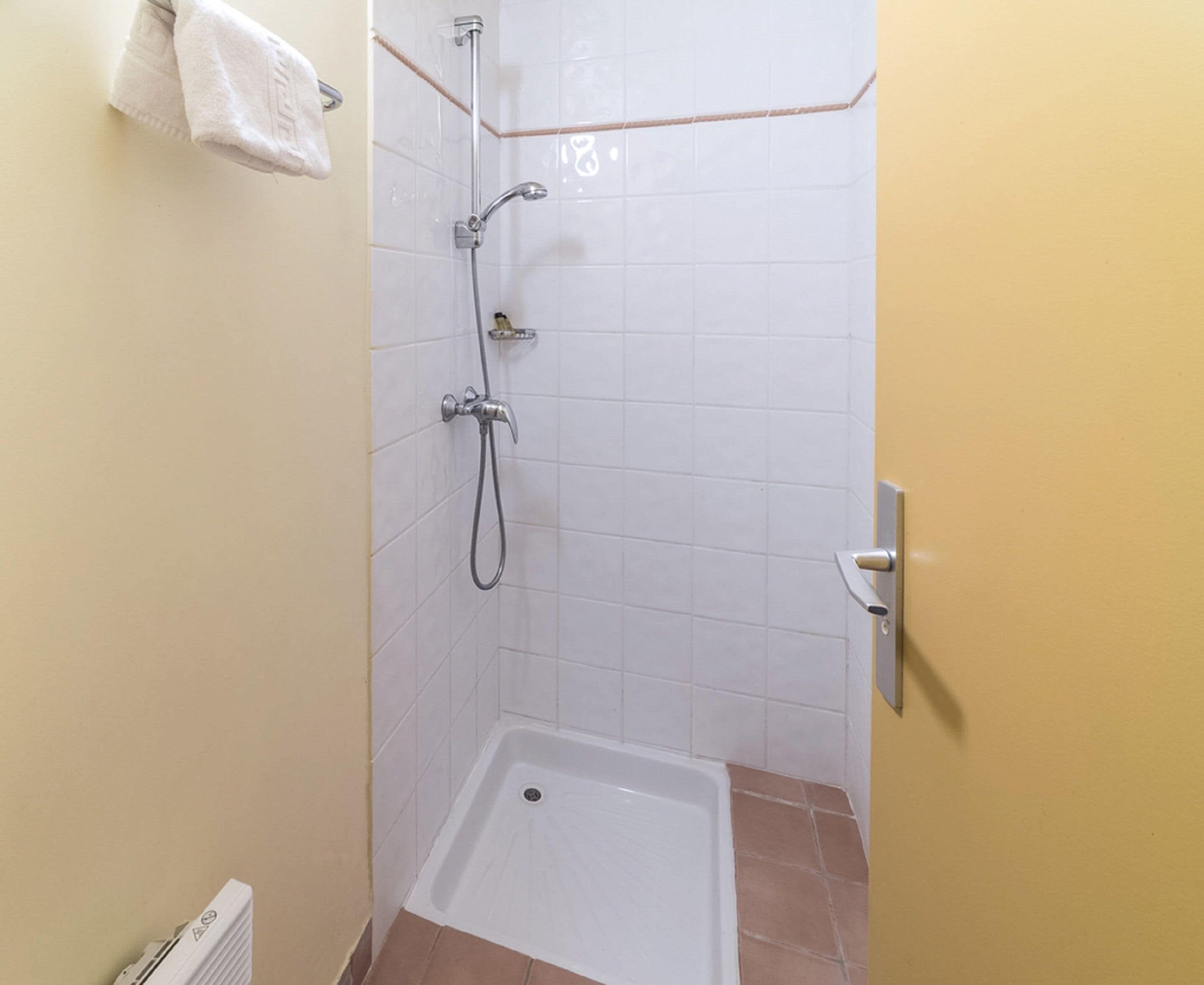 A small, enclosed shower area with a white bathtub, a handheld showerhead, and a wall-mounted faucet.