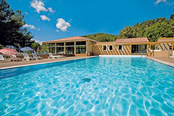 A swimming pool with lounge chairs and umbrellas, surrounded by buildings with a tiled roof.