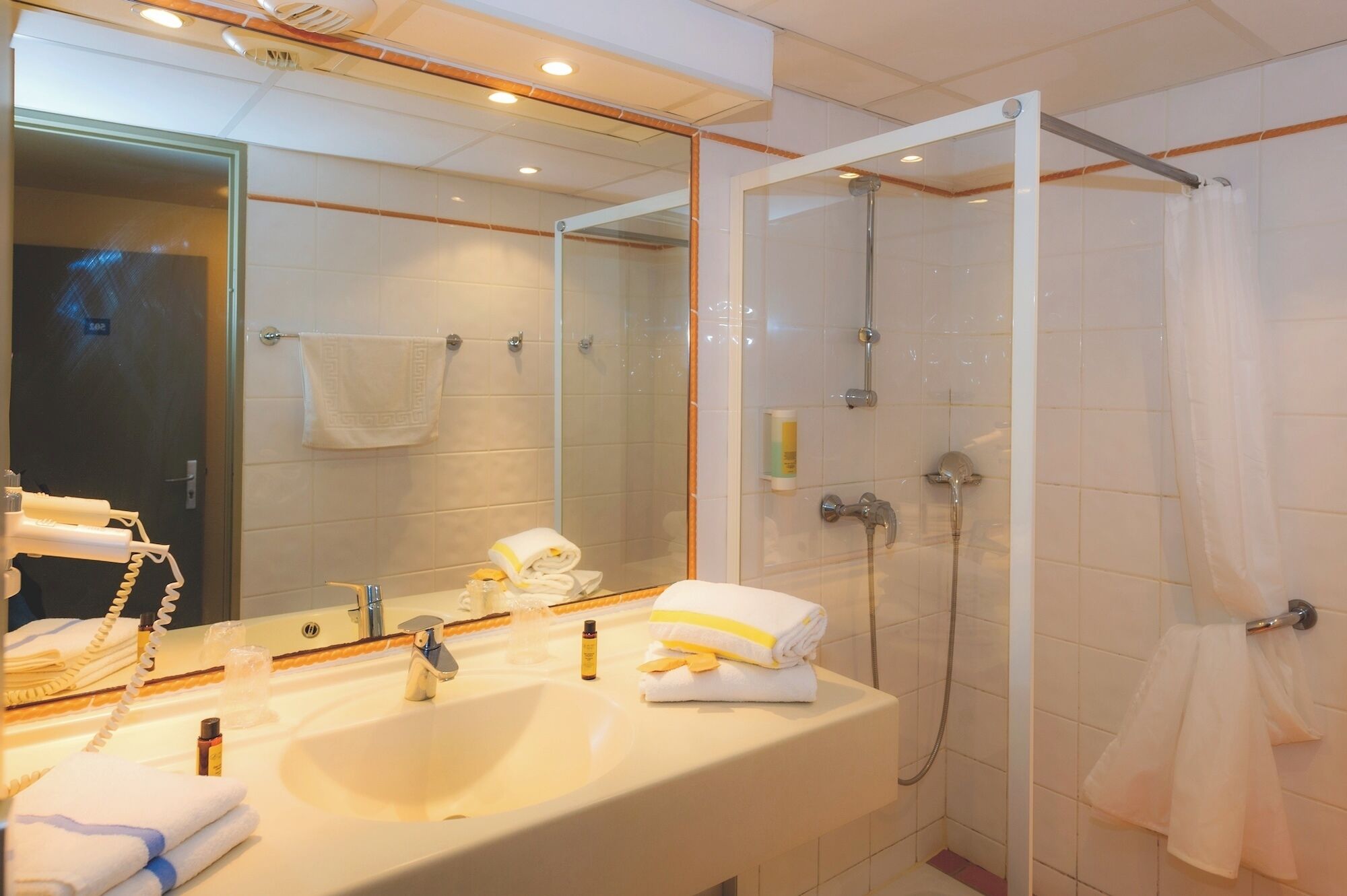 Un baño con lavamanos, espejo, ducha y toallero.