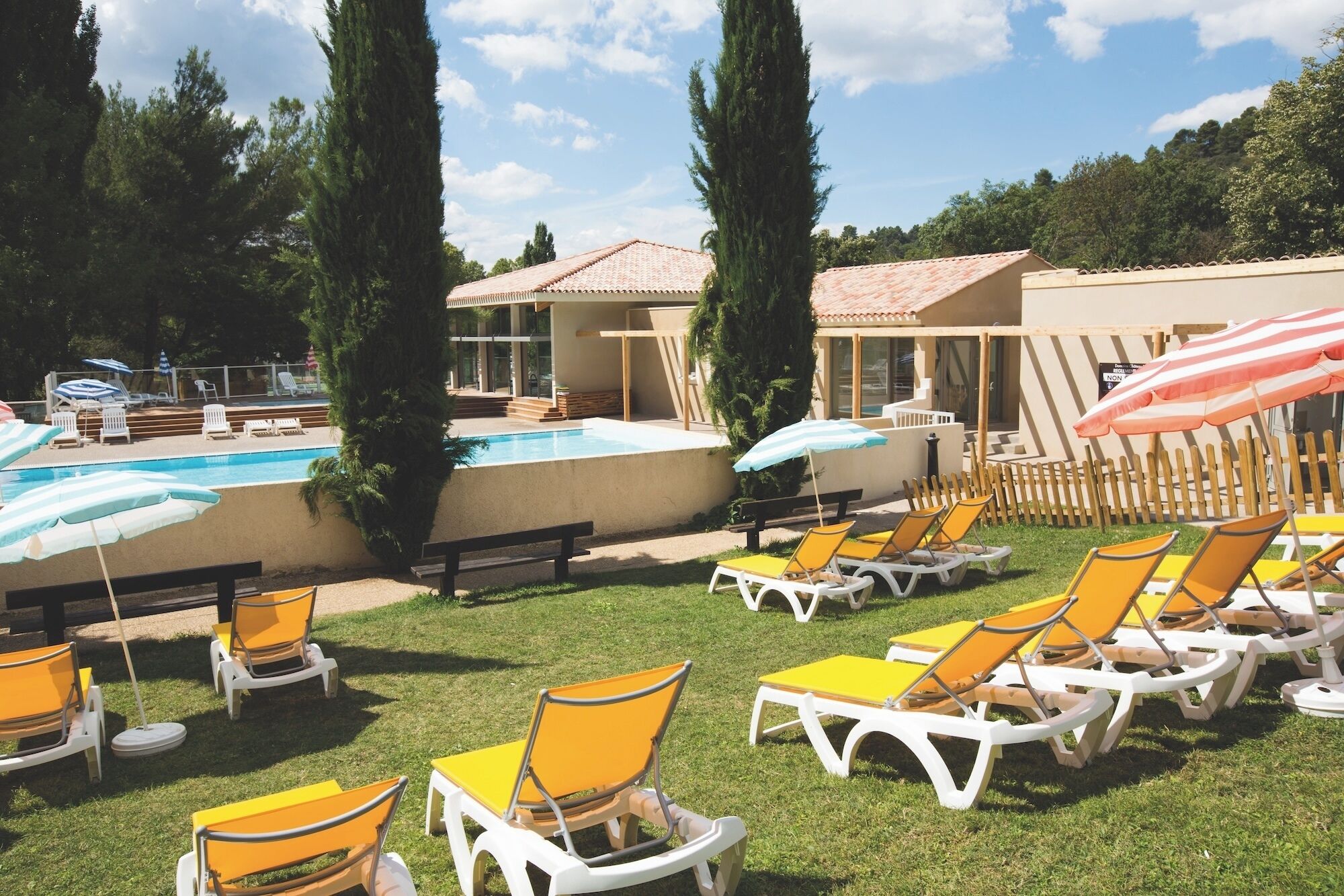 A pool area with lounge chairs and umbrellas, surrounded by greenery and buildings.