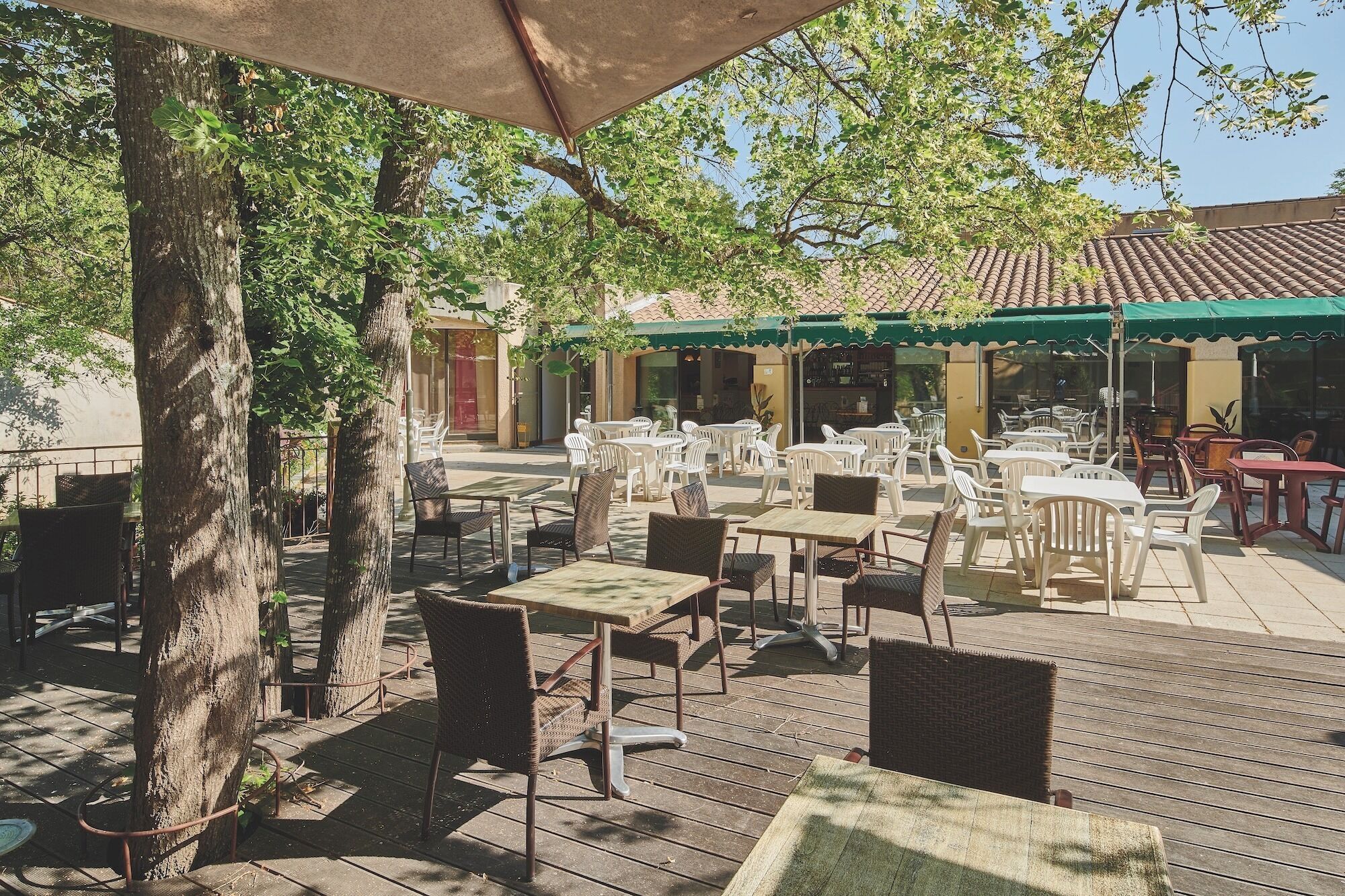 An outdoor patio with tables and chairs, a covered area, and a building with a tiled roof in the background.