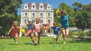 Eine Gruppe von Kindern spielt auf einer Wiese, im Hintergrund ein großes Gebäude.