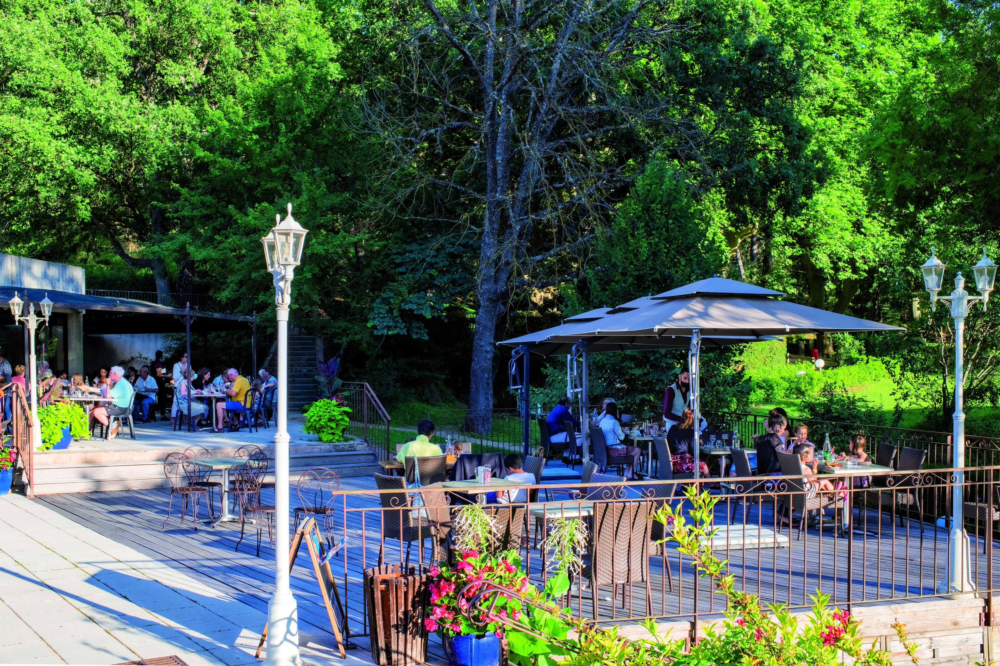 An outdoor patio area with tables and chairs, surrounded by greenery and trees.