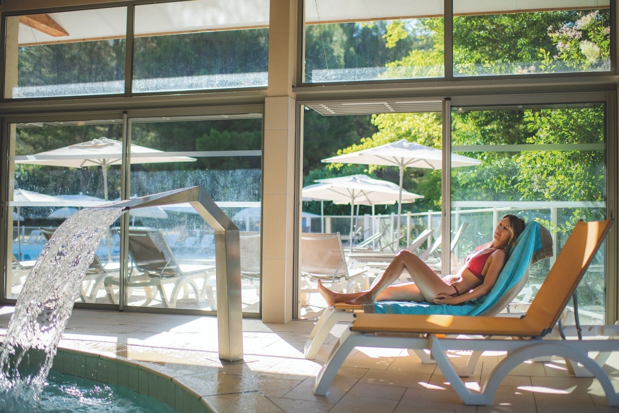 Área de piscina com um elemento aquático, espreguiçadeiras e guarda-sóis.