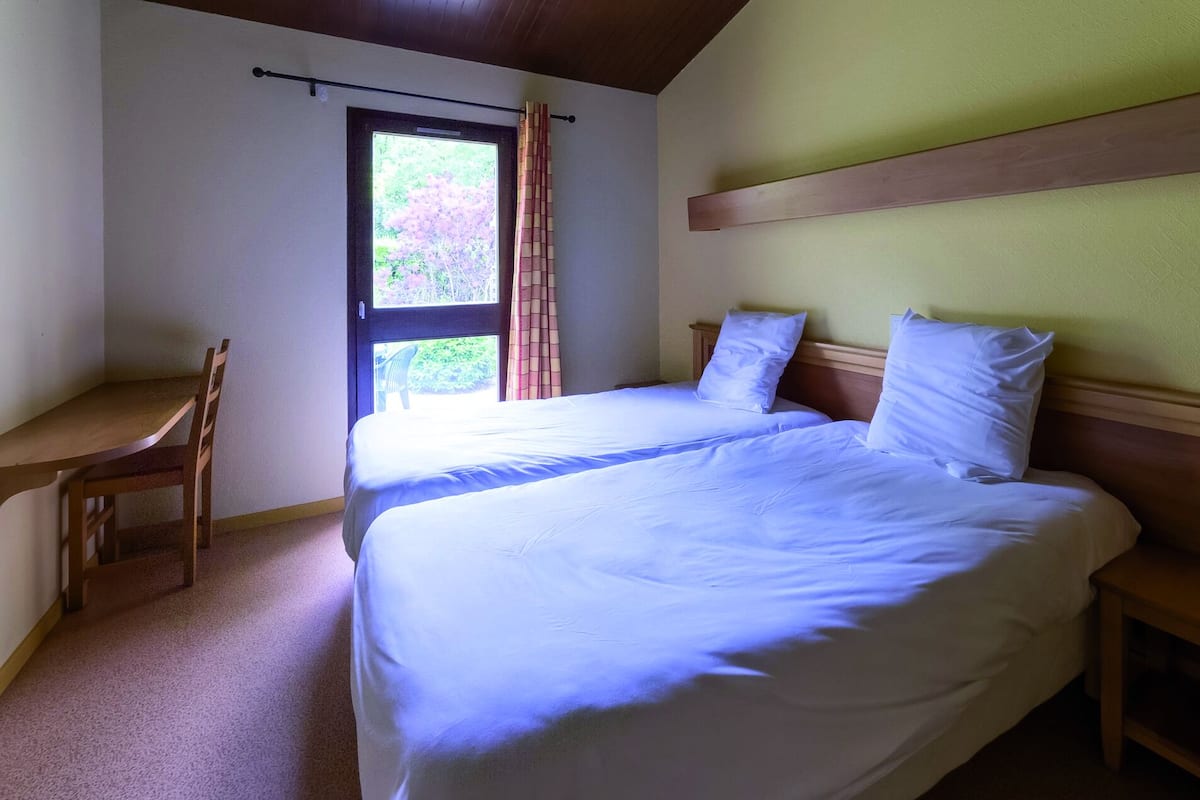 A bedroom with a bed, a desk, and a window with curtains.