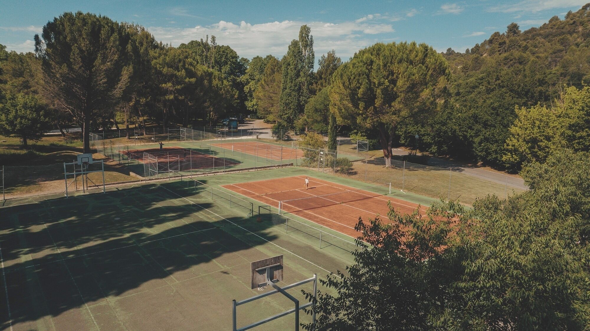A tennis court surrounded by trees and a hilly landscape.