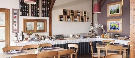 Un restaurante con mesas y sillas de madera, una barra larga con botellas de vino y cuadros en las paredes.
