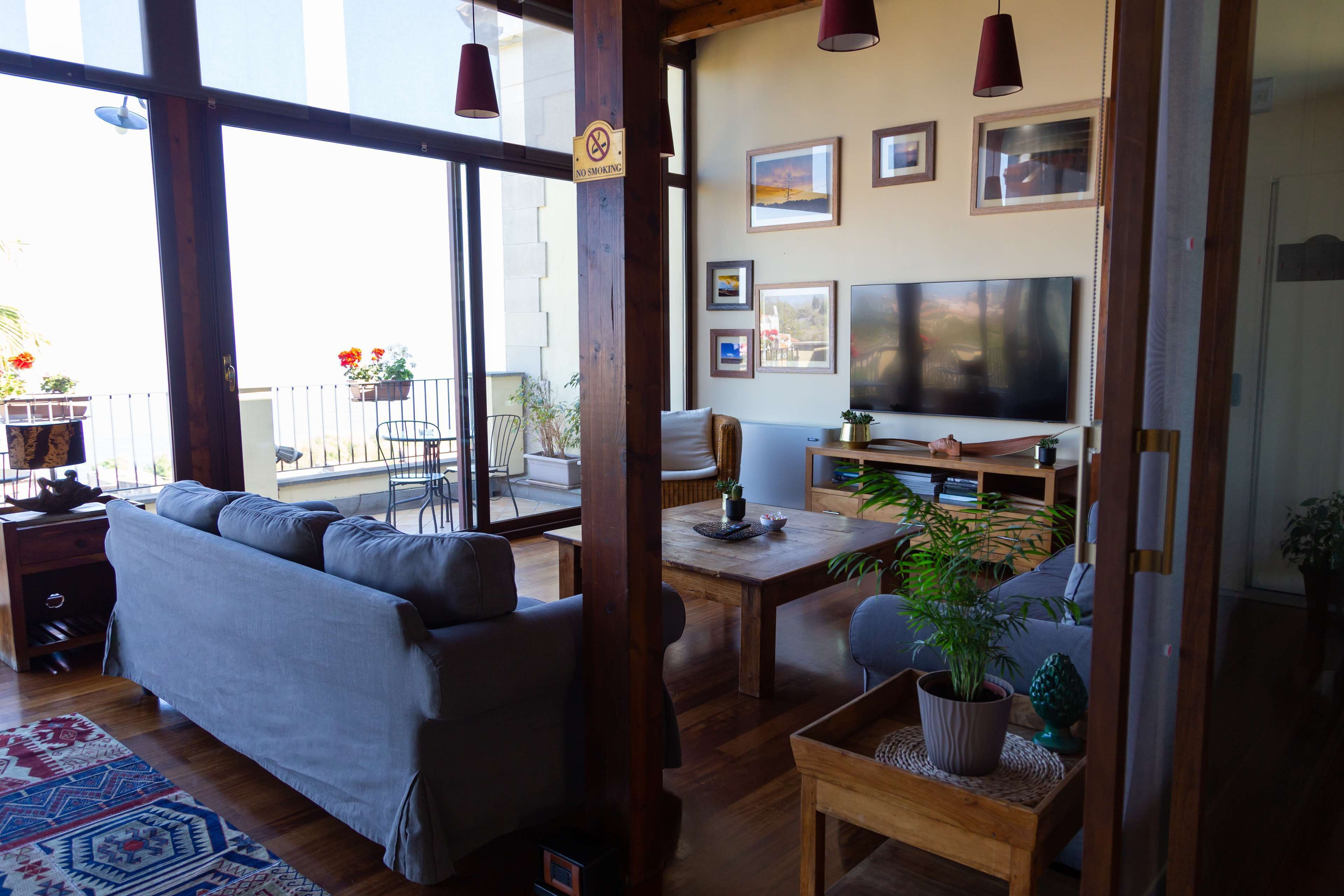 Un salón con sofá, mesa de comedor y televisor. Hay plantas y cuadros en las paredes.