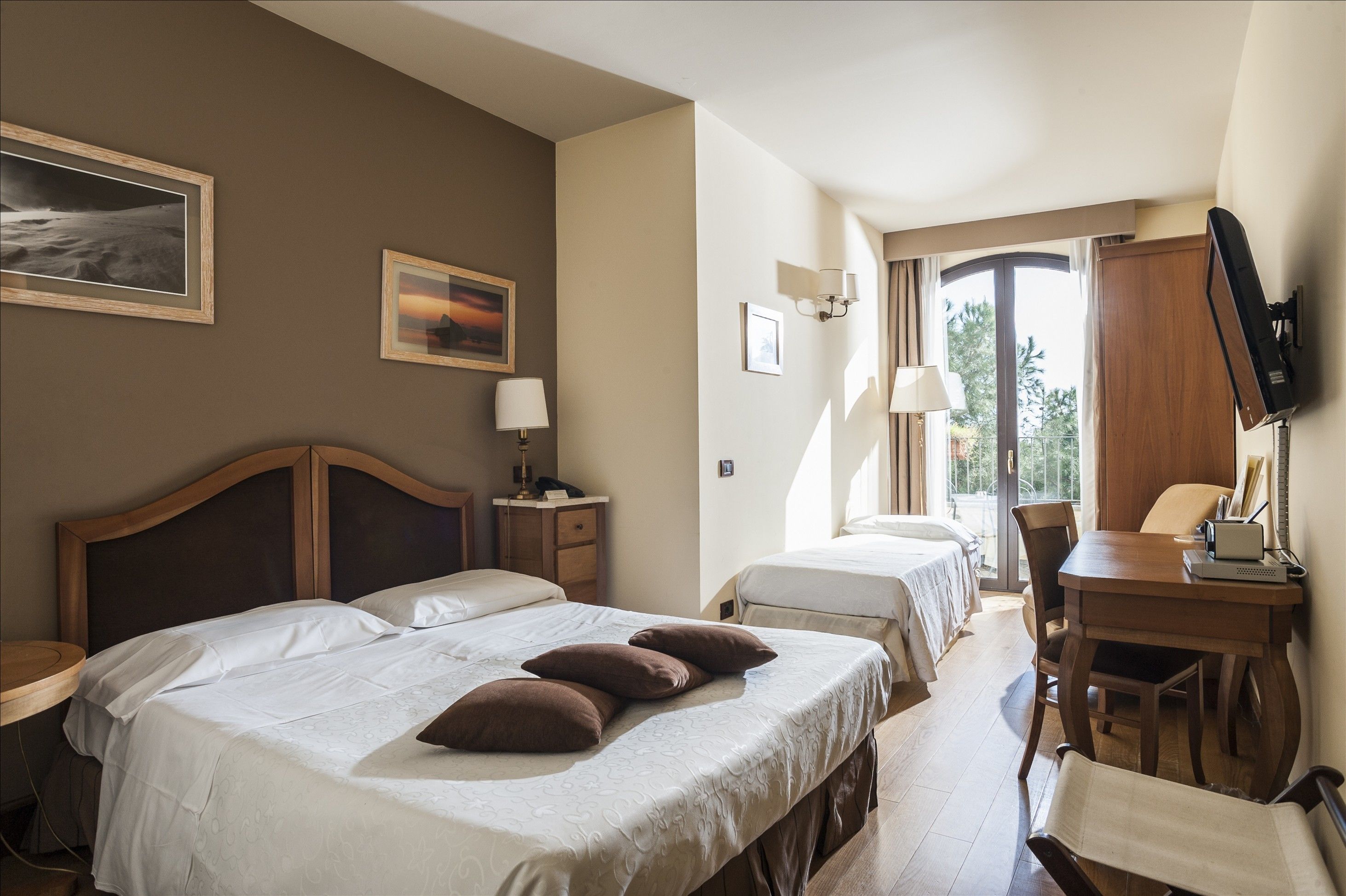 Habitación de hotel con dos camas, un escritorio, una silla, un televisor y una ventana con vistas.