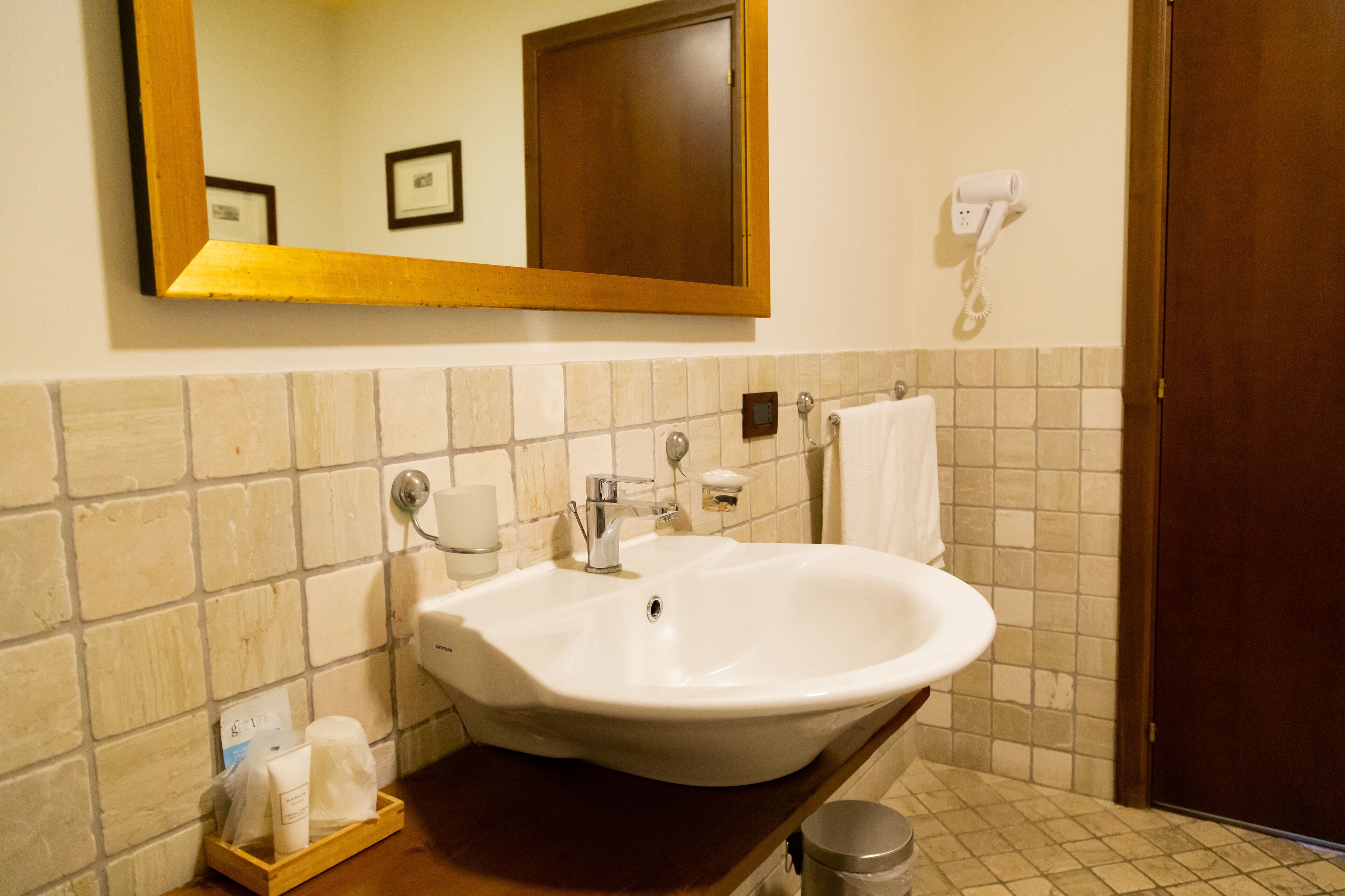 Ein Badezimmer mit einem weißen Waschbecken, einem Spiegel, einem Handtuchhalter und einem Föhn an der Wand.