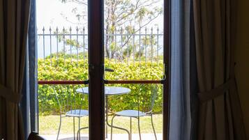 Un balcon avec deux chaises et une table en métal, une clôture en métal blanche, et une vue sur la verdure et les arbres.