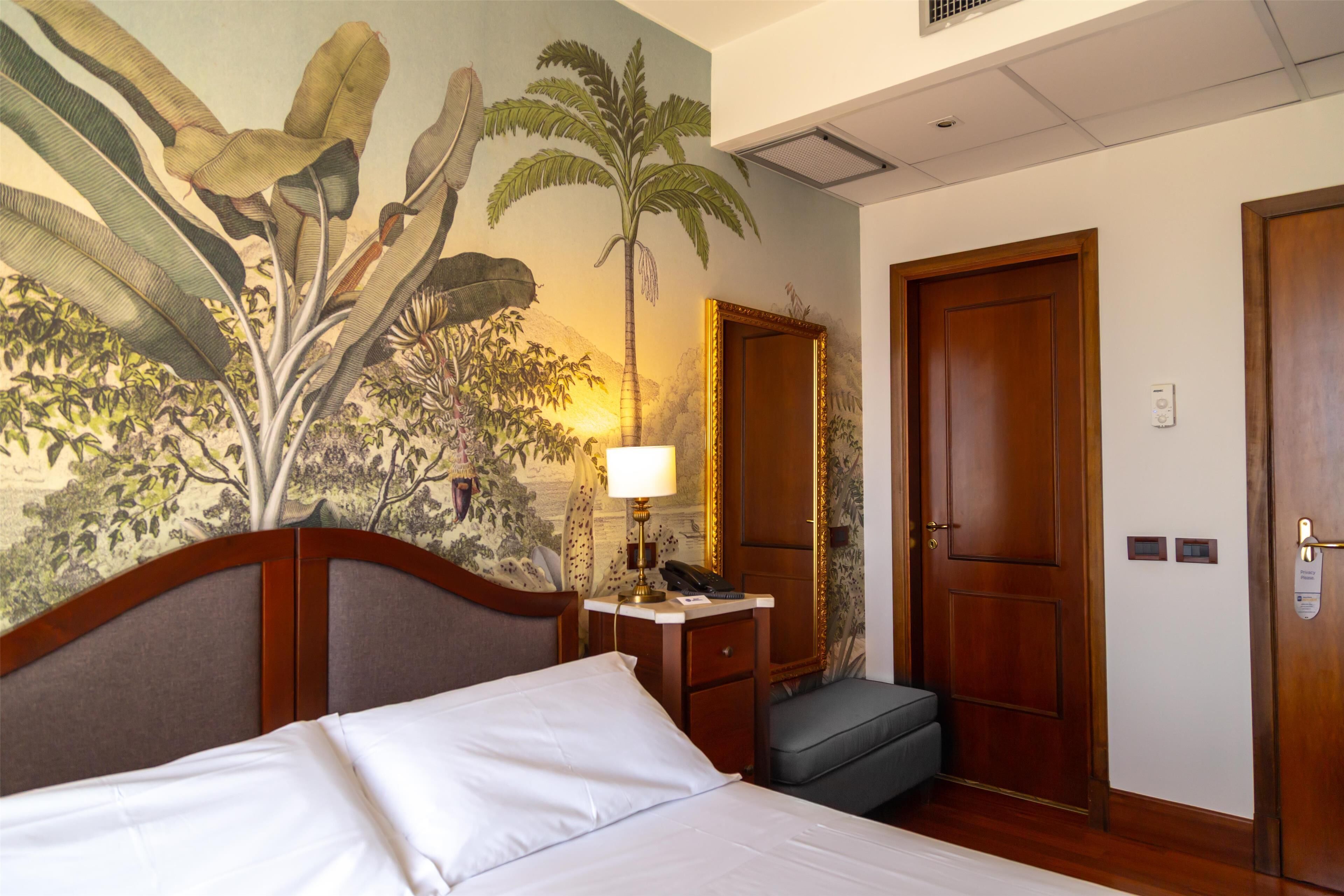 Una habitación de hotel con cama, mesita de noche, lámpara, silla y puerta.