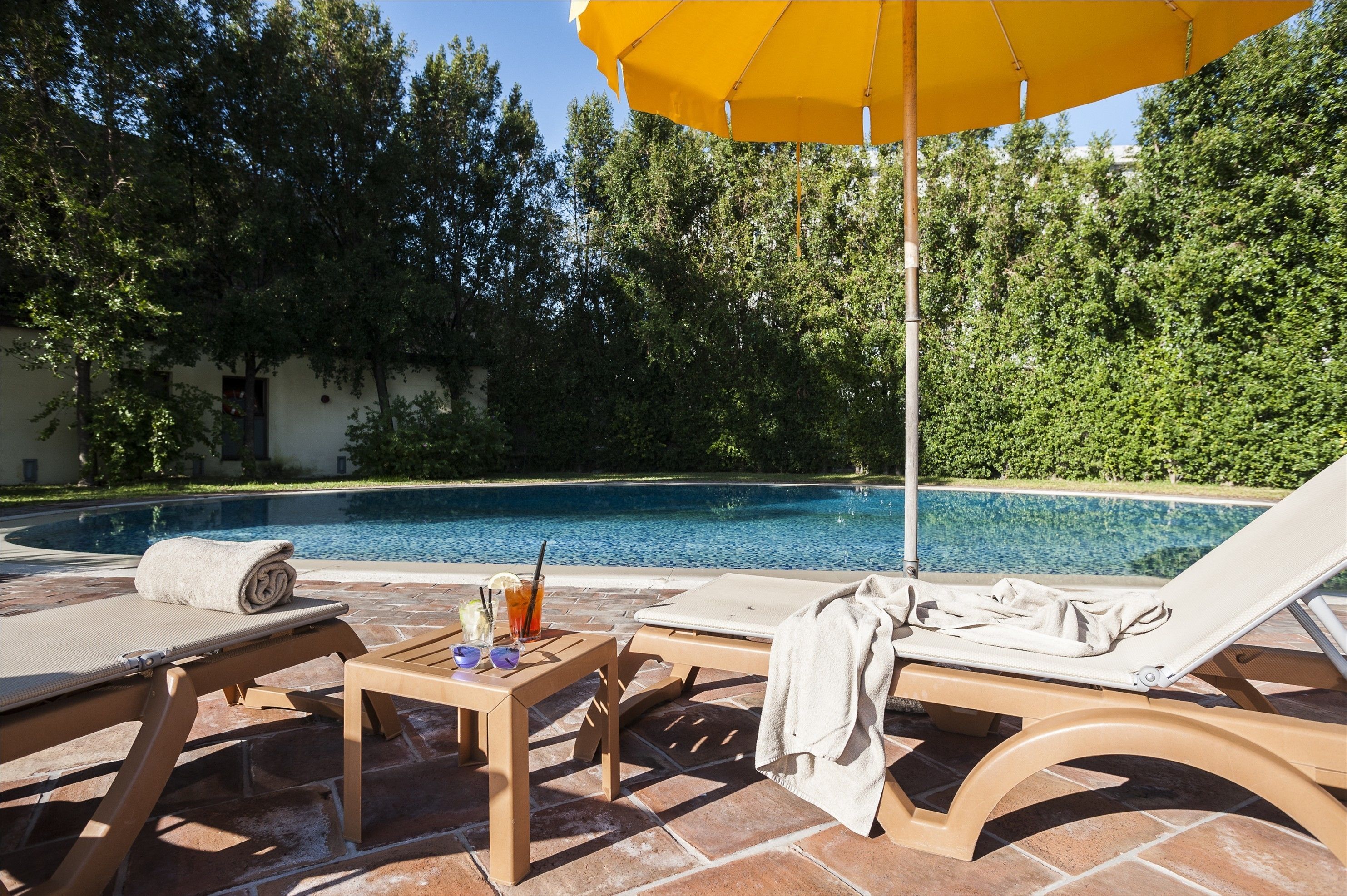 Zona junto a la piscina con sillones de descanso, una mesa con una toalla y un paraguas amarillo.