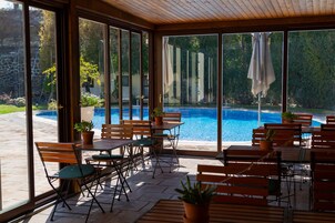 Zona relax all'aperto coperta, con tavoli e sedie, affacciata su una piscina.