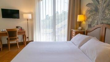 Una camera d'albergo con un letto, una scrivania, una sedia, una televisione e una finestra con tende.