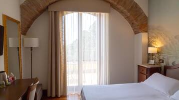 Habitación de hotel con cama, escritorio, silla, lámpara y ventana con cortinas.