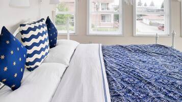 Un dormitorio con una cama, dos lámparas de noche y tres ventanas con cortinas.