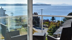 A balcony with wicker furniture overlooking a body of water and distant land. - Star of the Sea Guest House (White Rock)