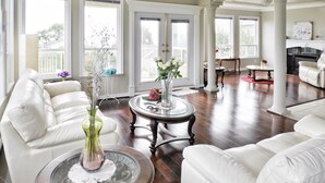 A spacious living room with white leather sofas, a glass coffee table, and a fireplace. - Star of the Sea Guest House (White Rock)