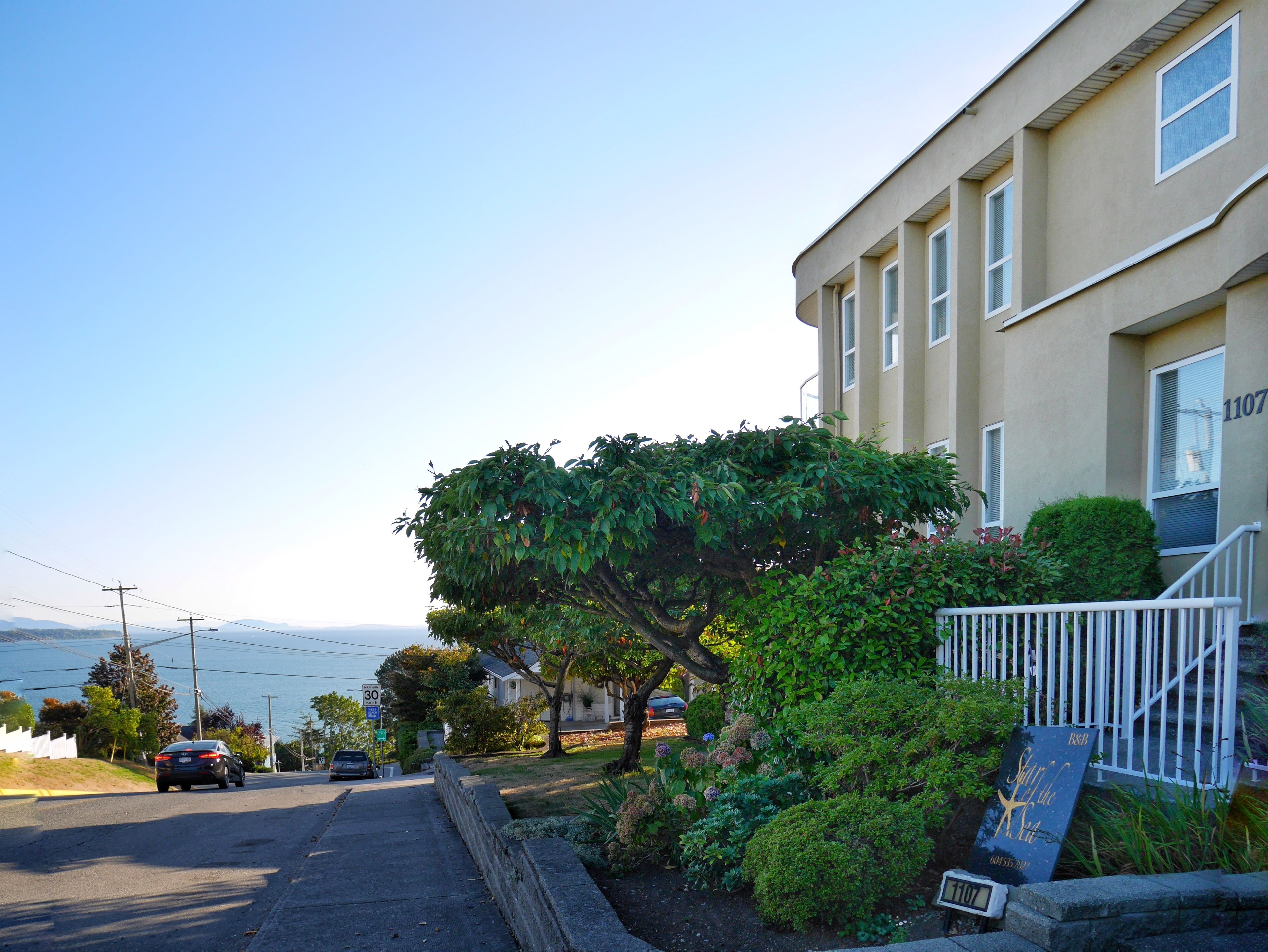Une rue résidentielle bordée de maisons, dont certaines possèdent un petit jardin et offrent une vue sur l’eau.