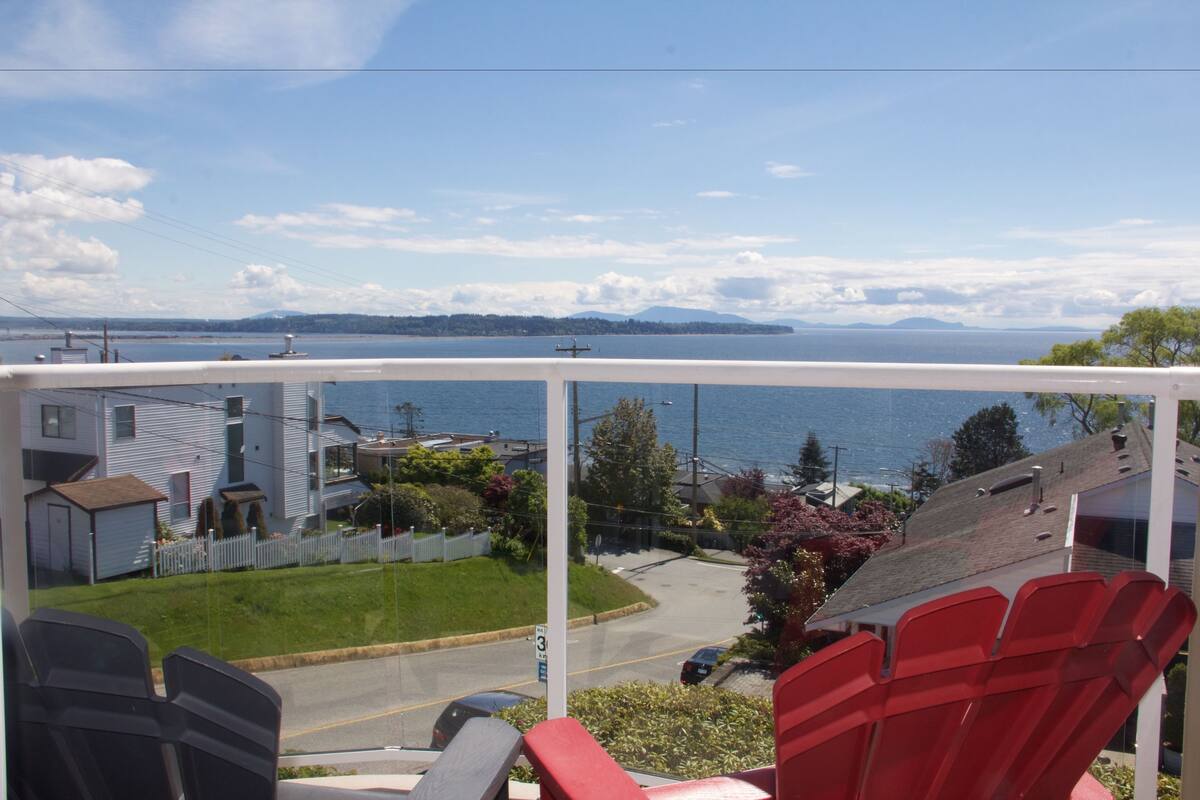 A balcony with a view of a residential area and a body of water.