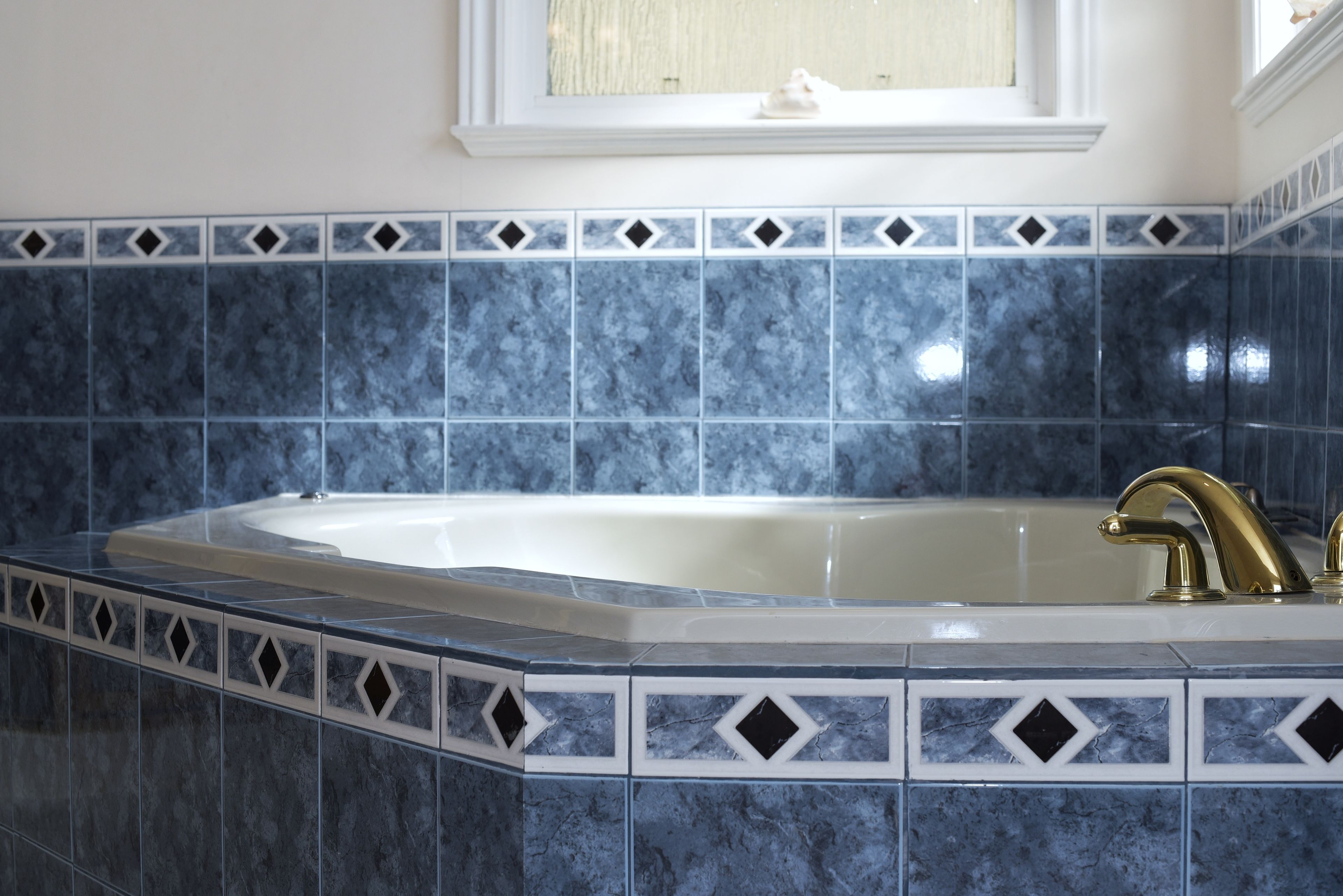 A bathroom with a freestanding bathtub, a white sink, and blue marble tiles with diamond patterns.