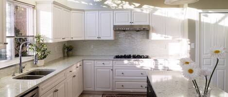 A modern kitchen with white cabinets, a stainless steel sink, and a gas stove.