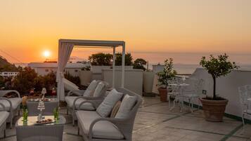 A rooftop terrace with wicker furniture, a table with drinks, and potted plants.