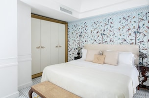 Un dormitorio con una cama grande, un armario, un banco y una pared decorada con un estampado de pájaros.