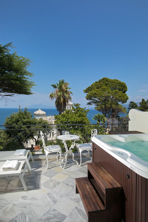 A rooftop terrace with a hot tub, white outdoor furniture, and a view of the sea and distant buildings. - Luxury Villa Excelsior Parco (Capri)