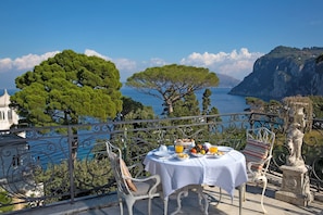 Una mesa dispuesta para el desayuno en un balcón con vistas a la costa, árboles y acantilados.