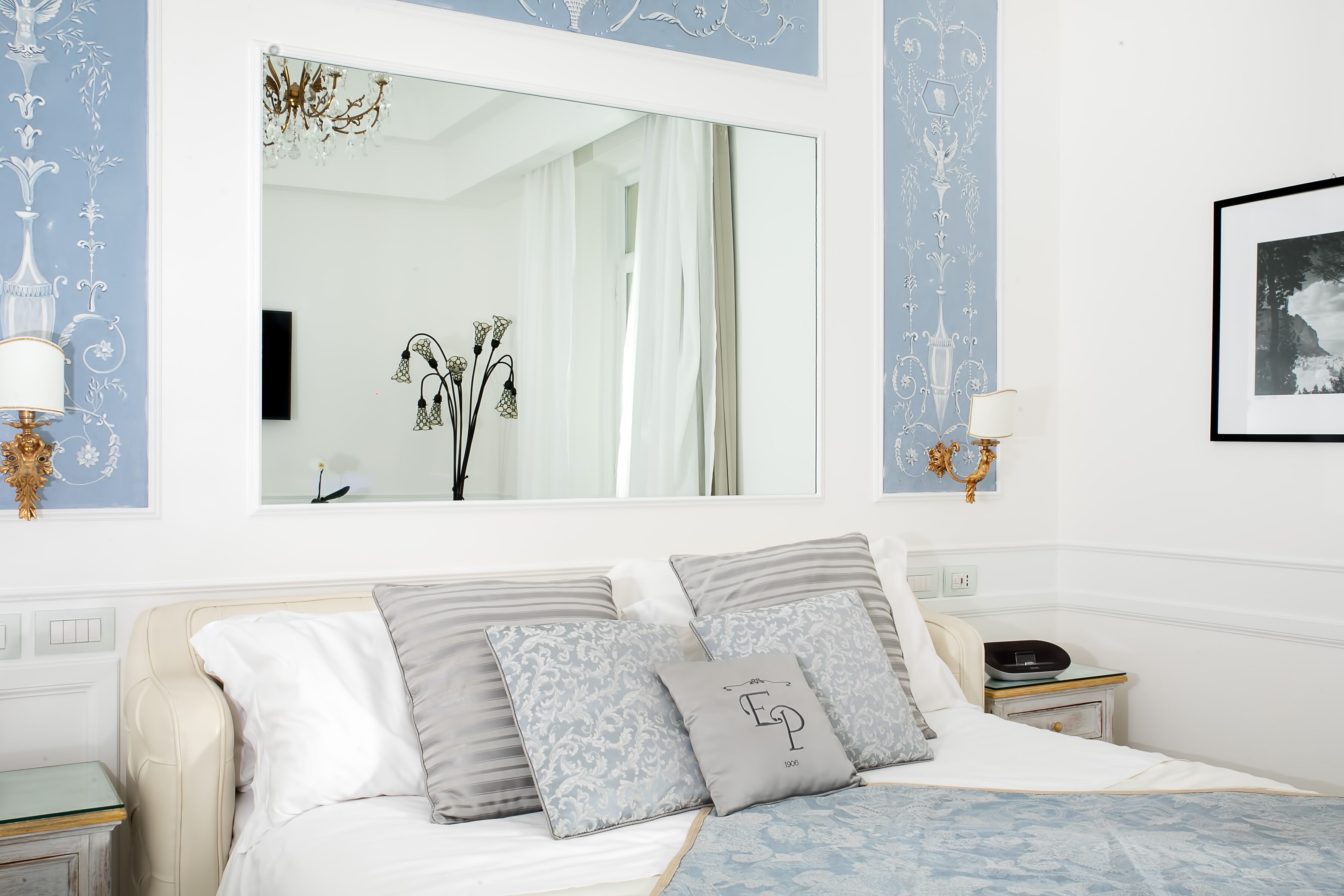 Une chambre à coucher avec un lit, des oreillers, une table de chevet, un miroir et des éléments de décoration murale.
