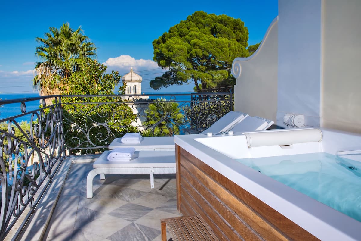 Un balcón con un jacuzzi, sillones de descanso y vista al mar y un edificio con cúpula.