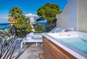 A balcony with a hot tub, lounge chairs, and a view of the sea and a building with a dome. - Luxury Villa Excelsior Parco (Capri)
