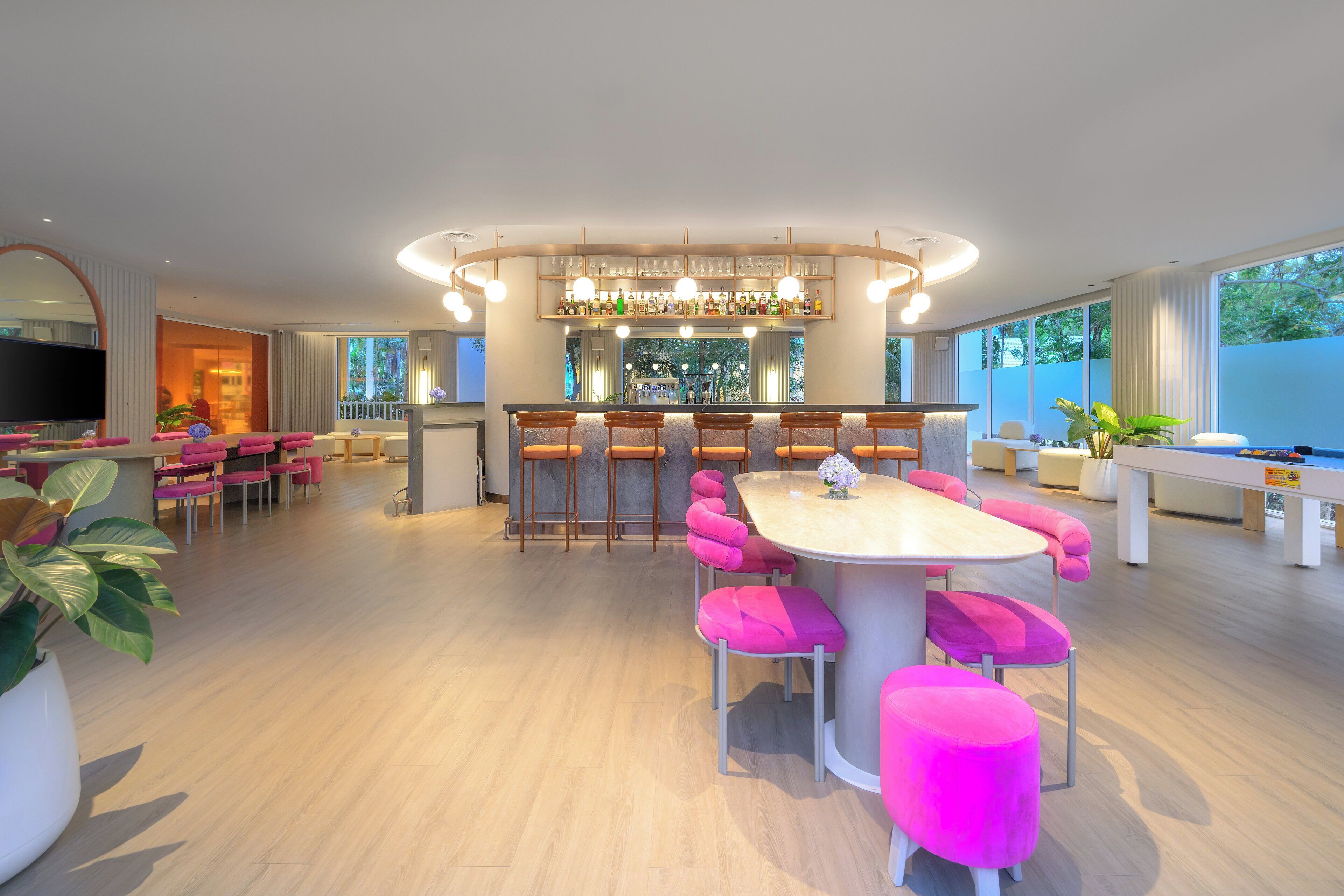 A modern kitchen with a central island, bar area with stools, and a seating area with pink chairs and ottomans.