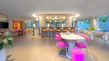 A modern kitchen with a central island, bar area with stools, and a seating area with pink chairs and ottomans.