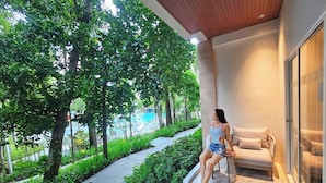 A woman sitting on a balcony with a view of a swimming pool and greenery. - Centara Karon Resort Phuket (Karon)