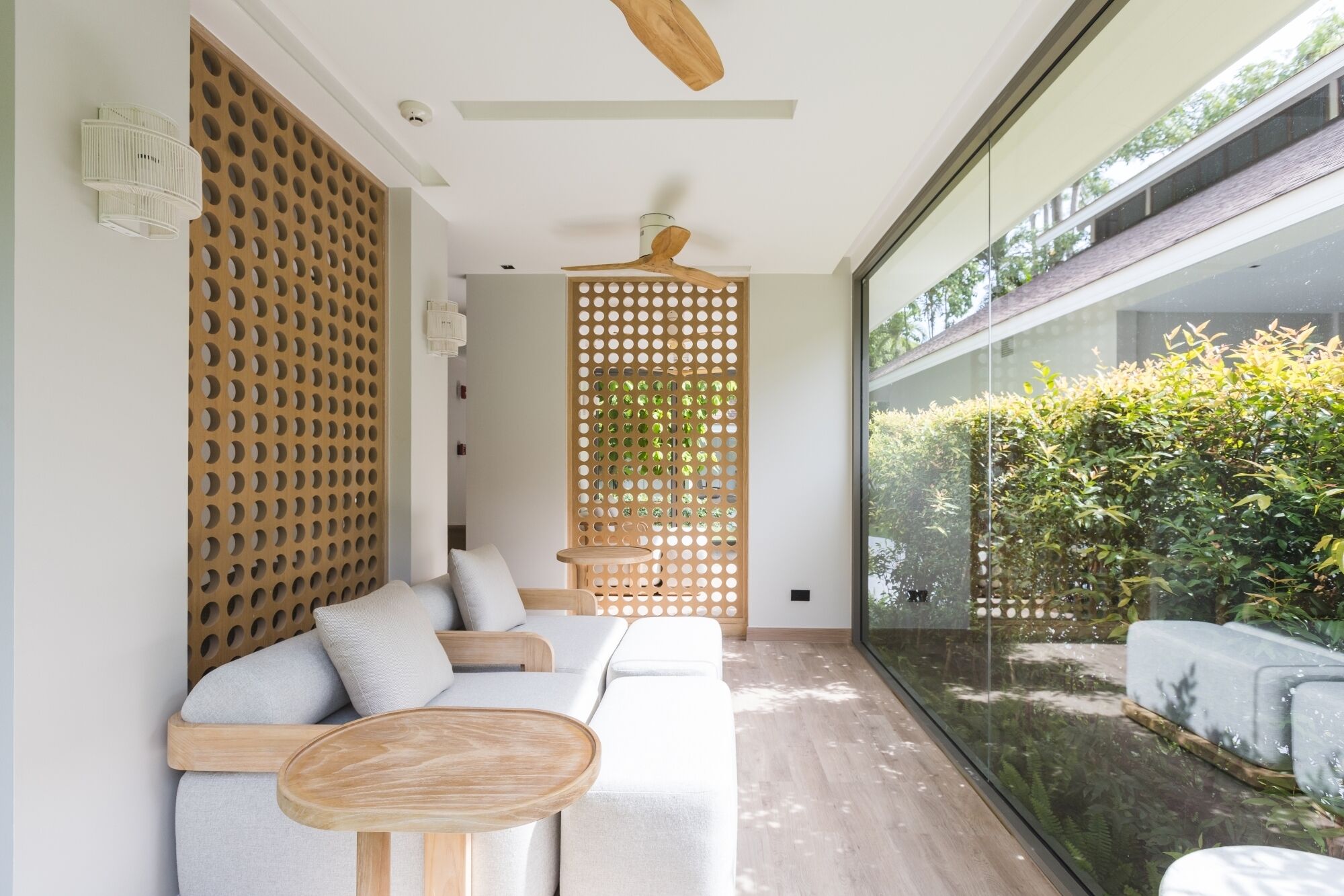 A modern interior with a wooden partition, a wooden ceiling fan, and a glass wall offering a view of greenery.