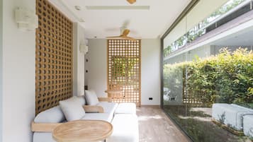 A modern interior with a wooden partition, a wooden ceiling fan, and a glass wall offering a view of greenery.