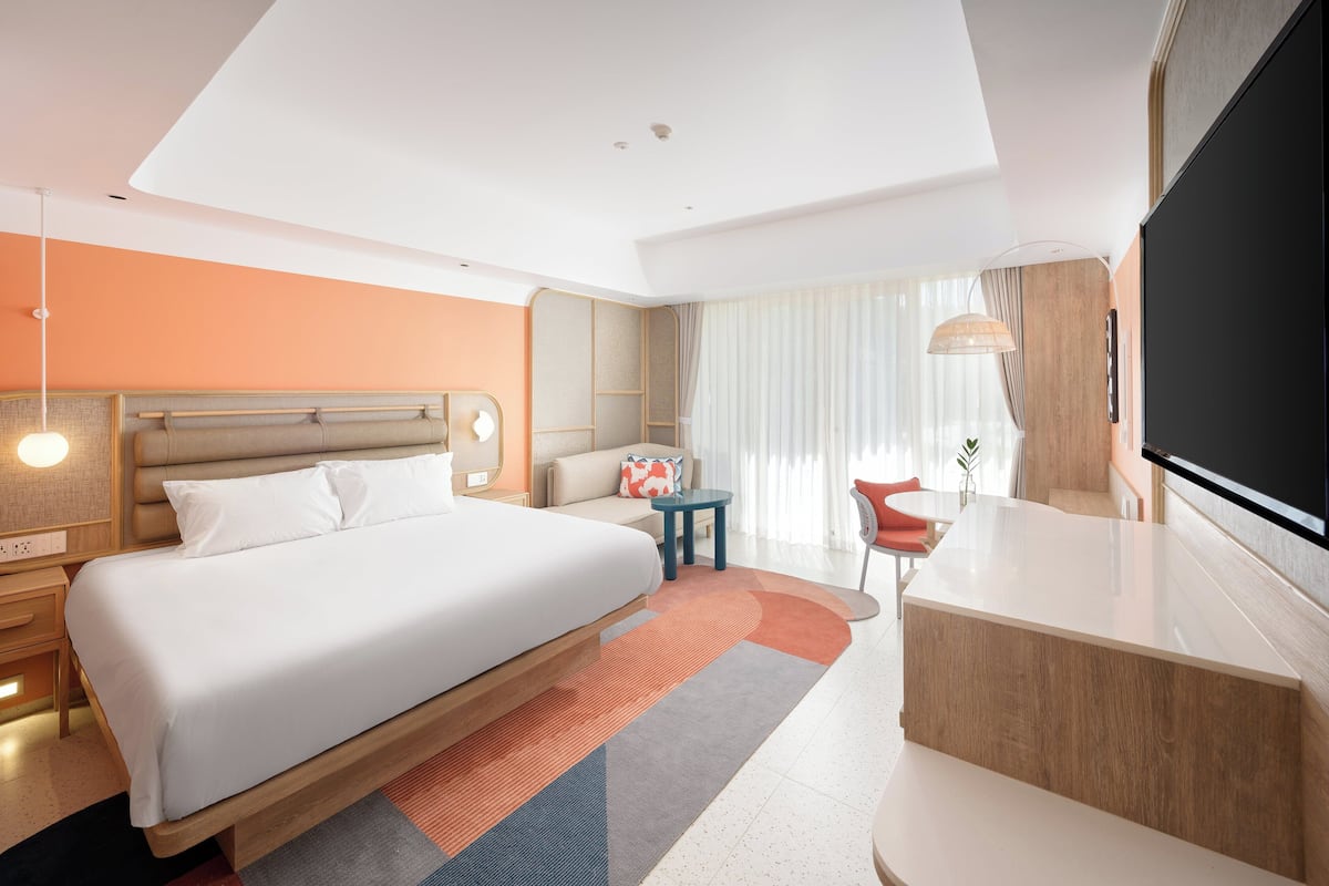 A modern hotel room with a large bed, a desk, a chair, and a TV.